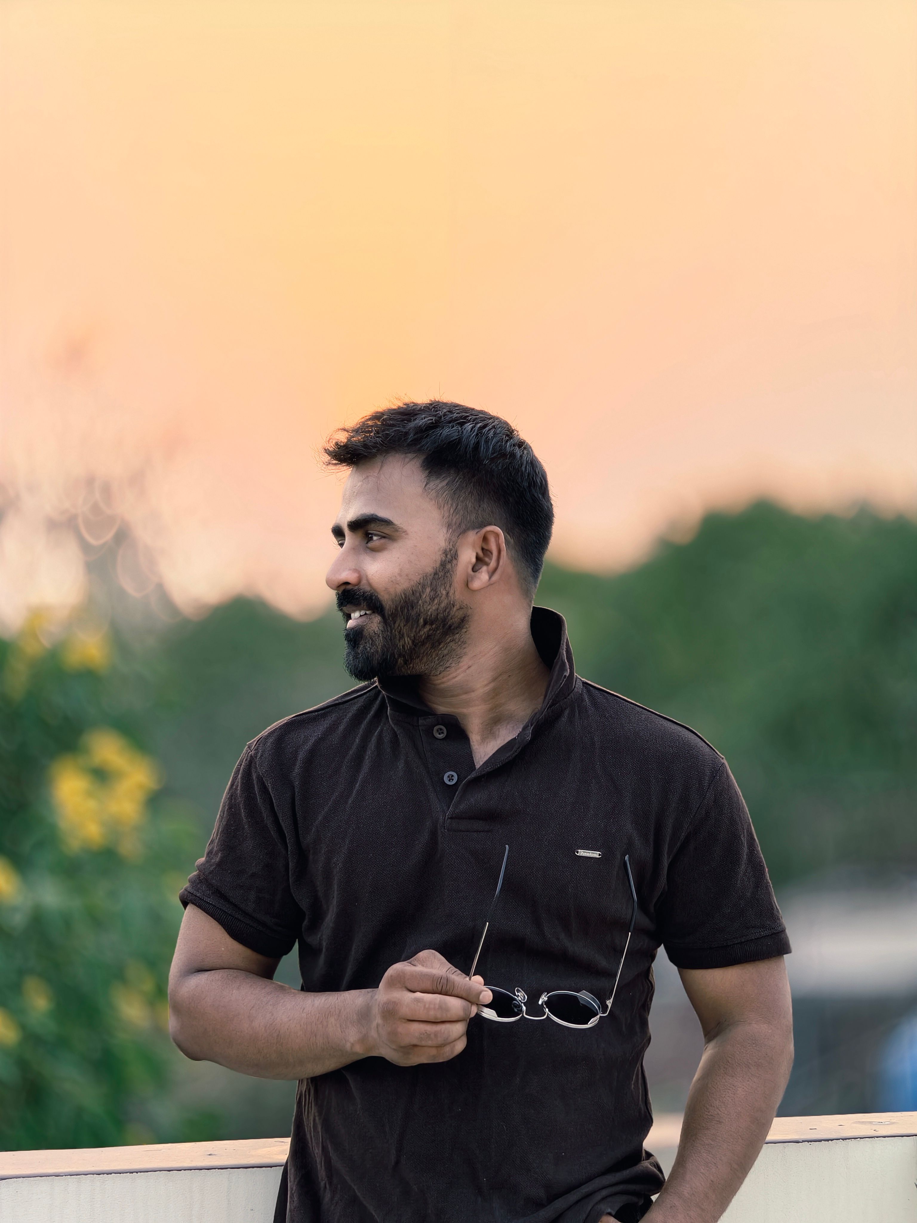 Portrait of a man holding glasses, enjoying a serene outdoor sunset view.