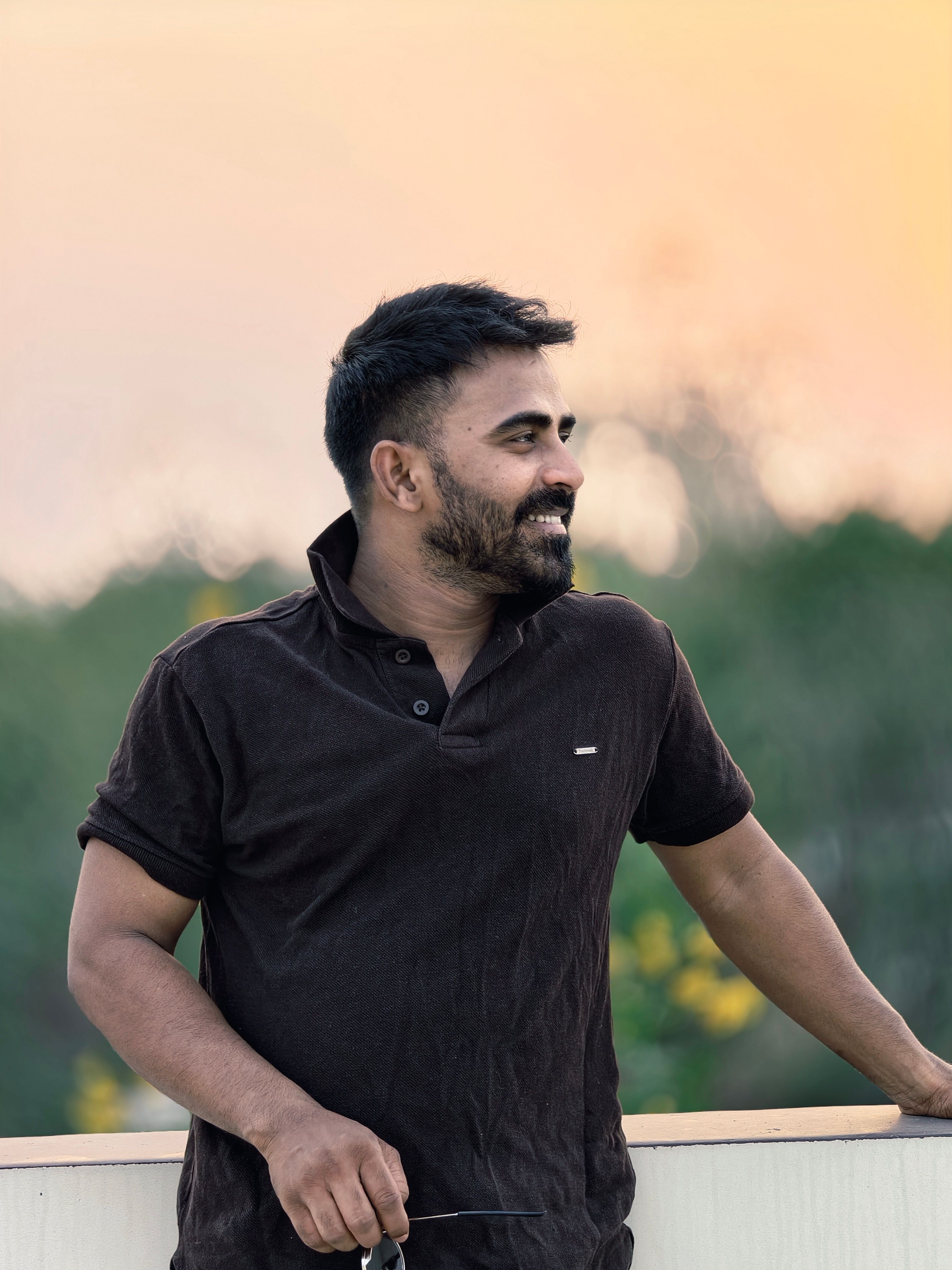 Portrait of a smiling man outdoors during a warm sunset, leaning on a railing.