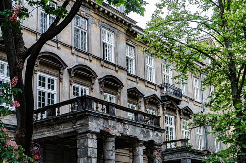 Free Vintage stone building facade with weathered columns and decorative windows surrounded by lush greenery. Stock Photo