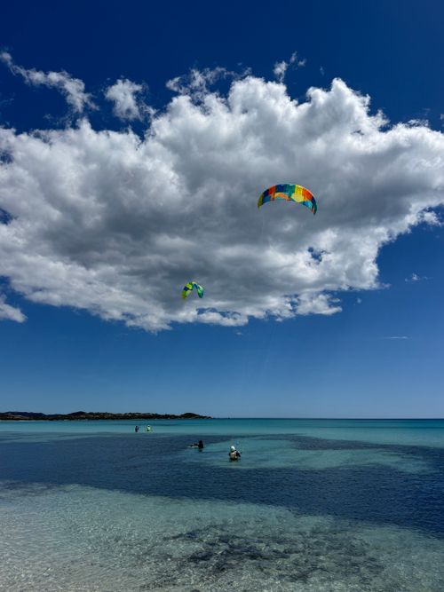 Free Experience the thrill of kitesurfing under dramatic clouds in Sardinia's crystal-clear waters. Stock Photo