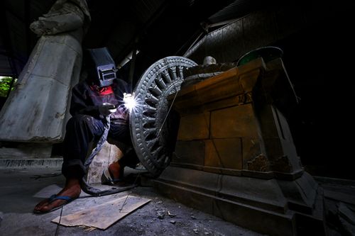 Free A welder crafts intricate details on a stone sculpture base in an Indonesian workshop. Stock Photo