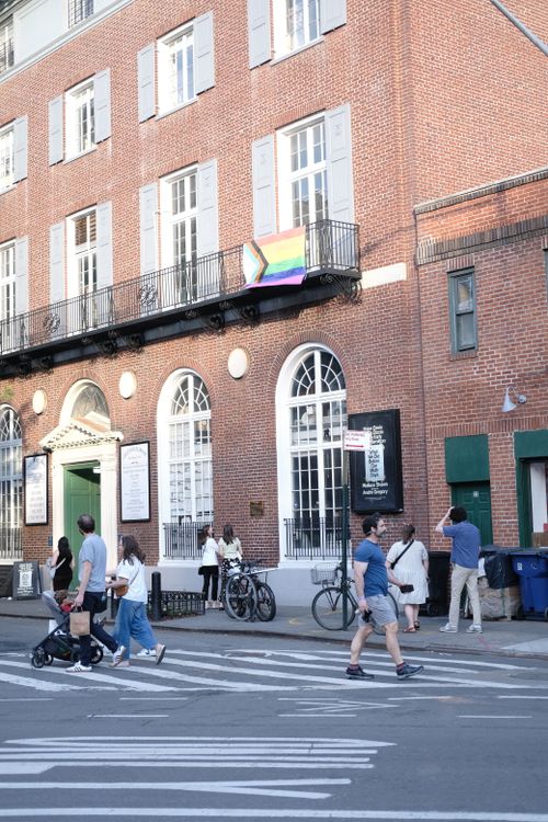 Free Urban street view with pedestrians and a diversity flag on a historic building facade. Stock Photo