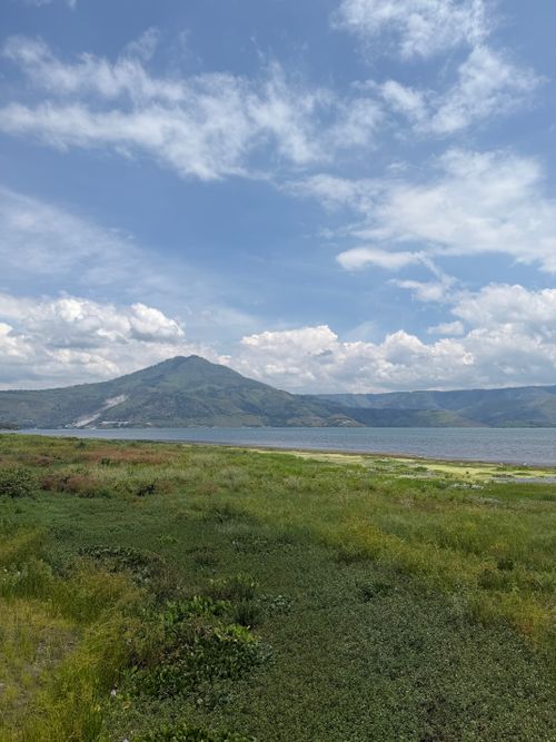 Free Expansive view of Lake Toba under a bright sky, showcasing rich vegetation and mountain backdrop. Stock Photo
