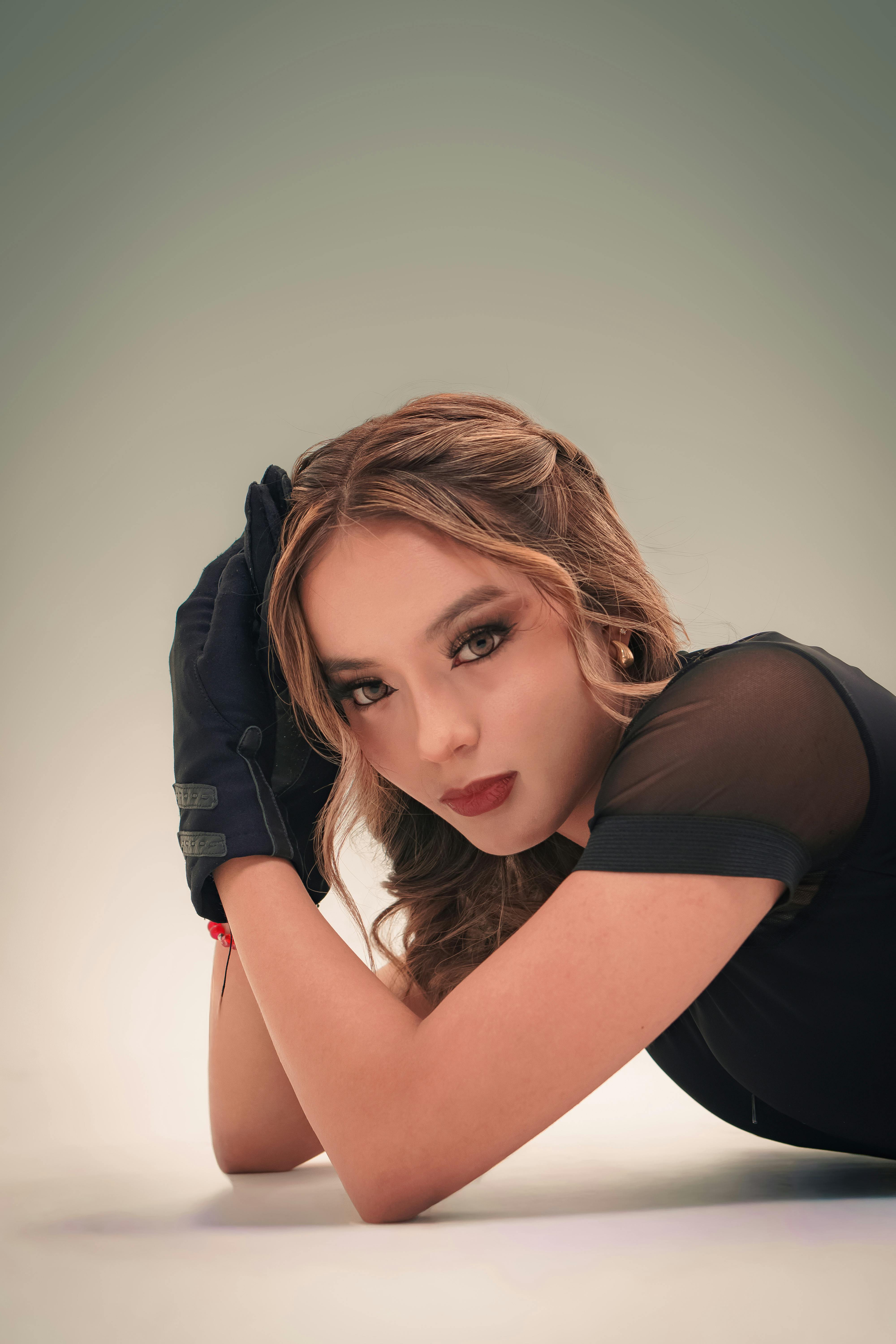 A stylish woman poses elegantly in a studio, showcasing modern fashion and makeup.