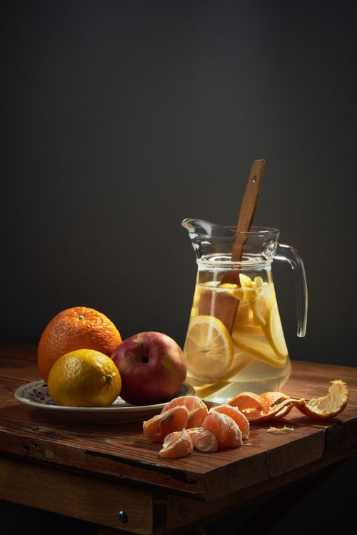 Free A still life photo of a jug of lemonade with lemons, oranges, and an apple on a wooden table. Stock Photo
