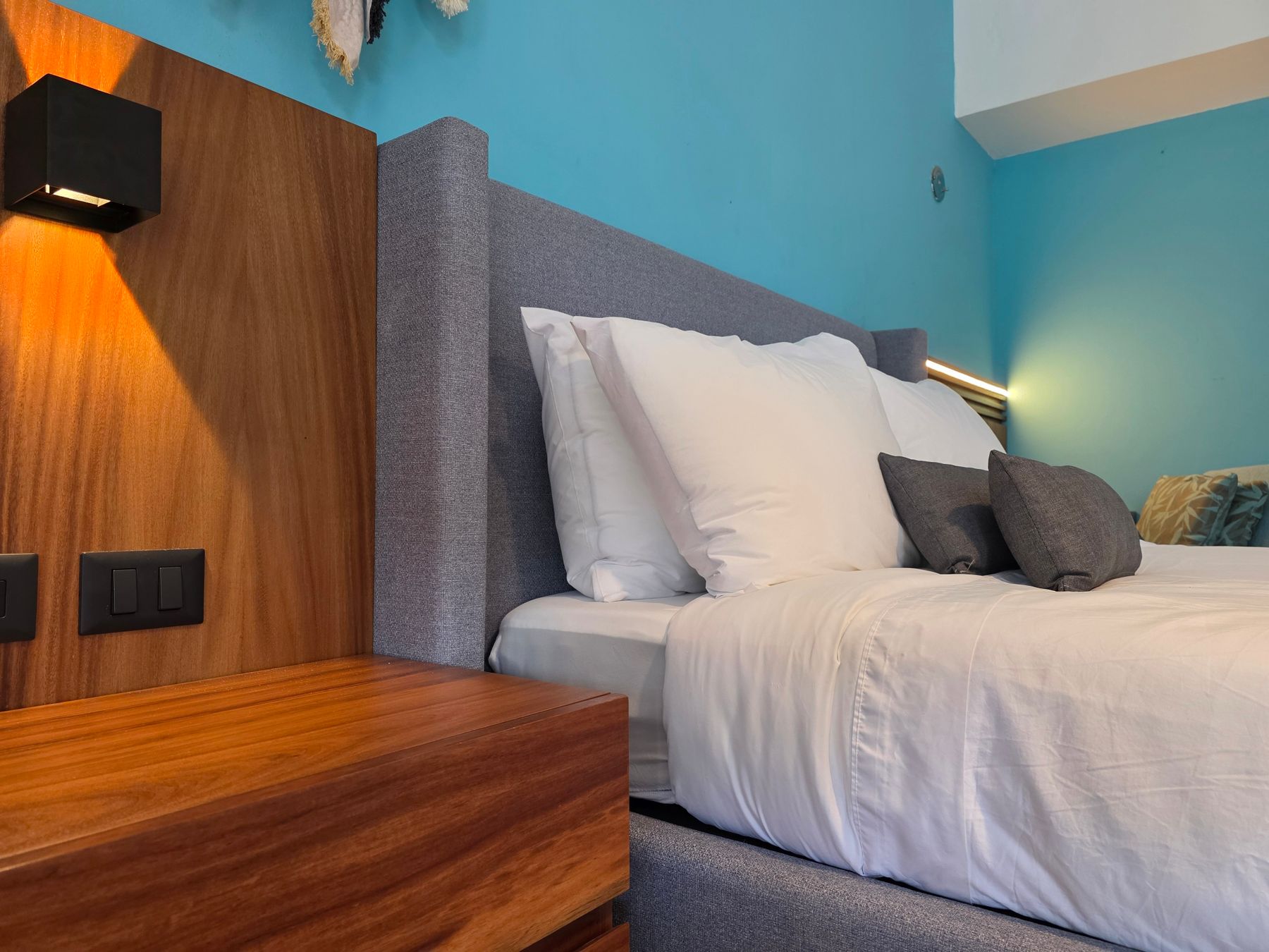 Modern bed with a wide gray upholstered headboard across blue and wood wall panels with reading lights