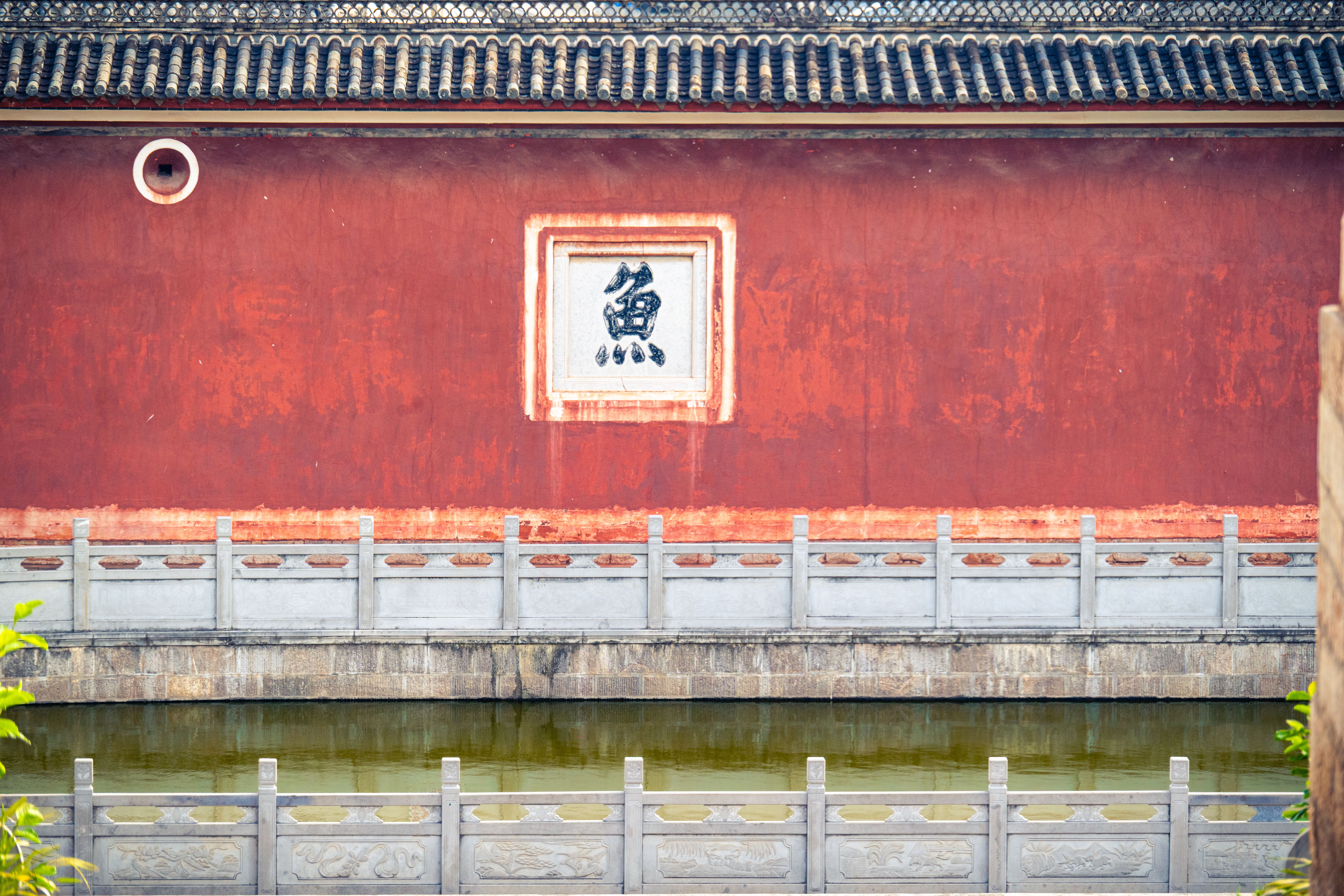 A serene shot of traditional Chinese architecture showcasing a red wall and reflective water.