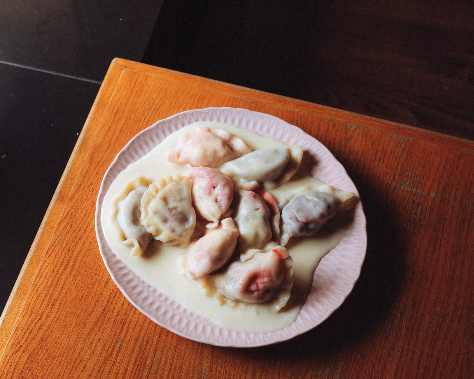 Colorful Polish pierogi dumplings served in a creamy sauce on a wooden table.