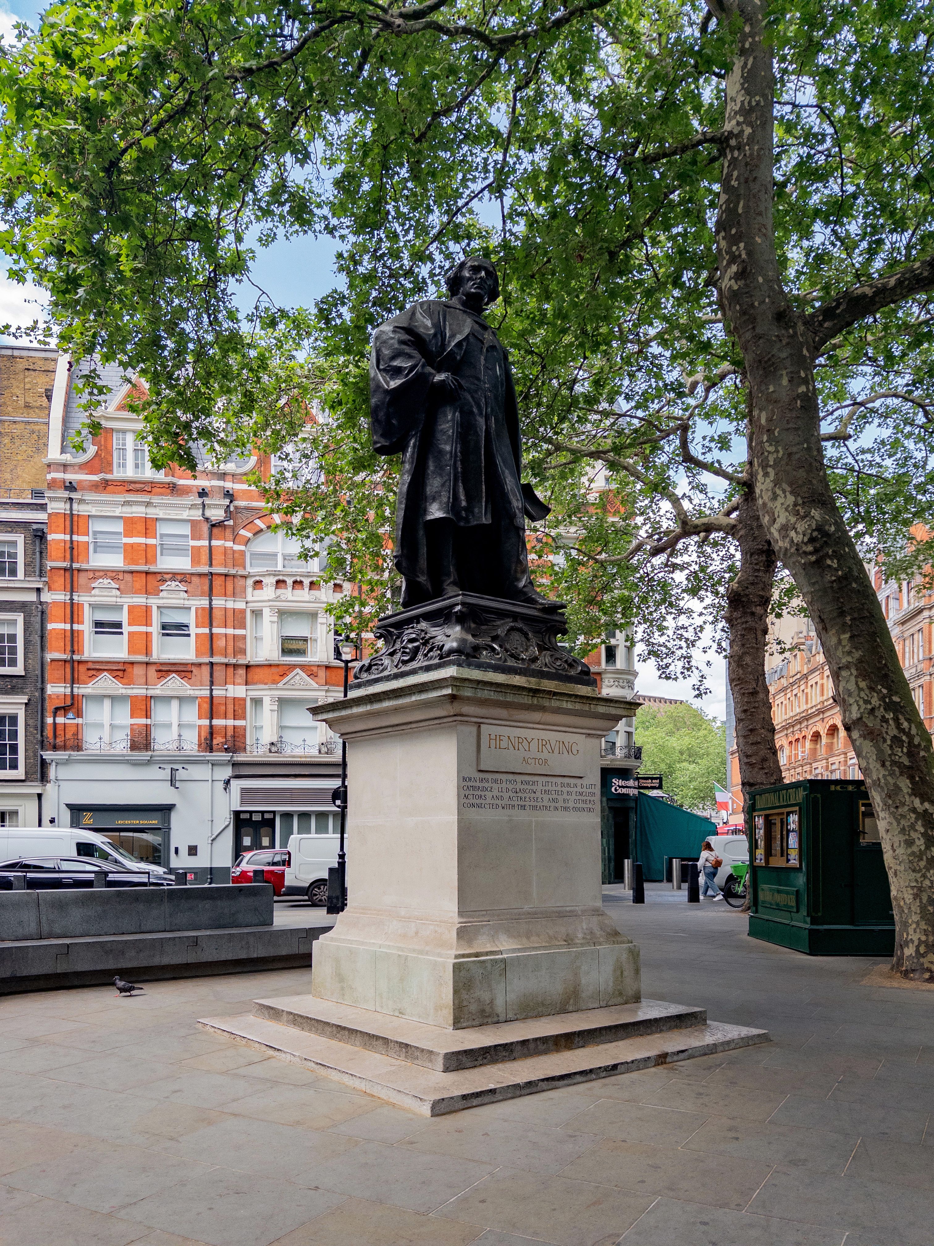Statue of Henry Irving located in a London square surrounded by trees and buildings.
