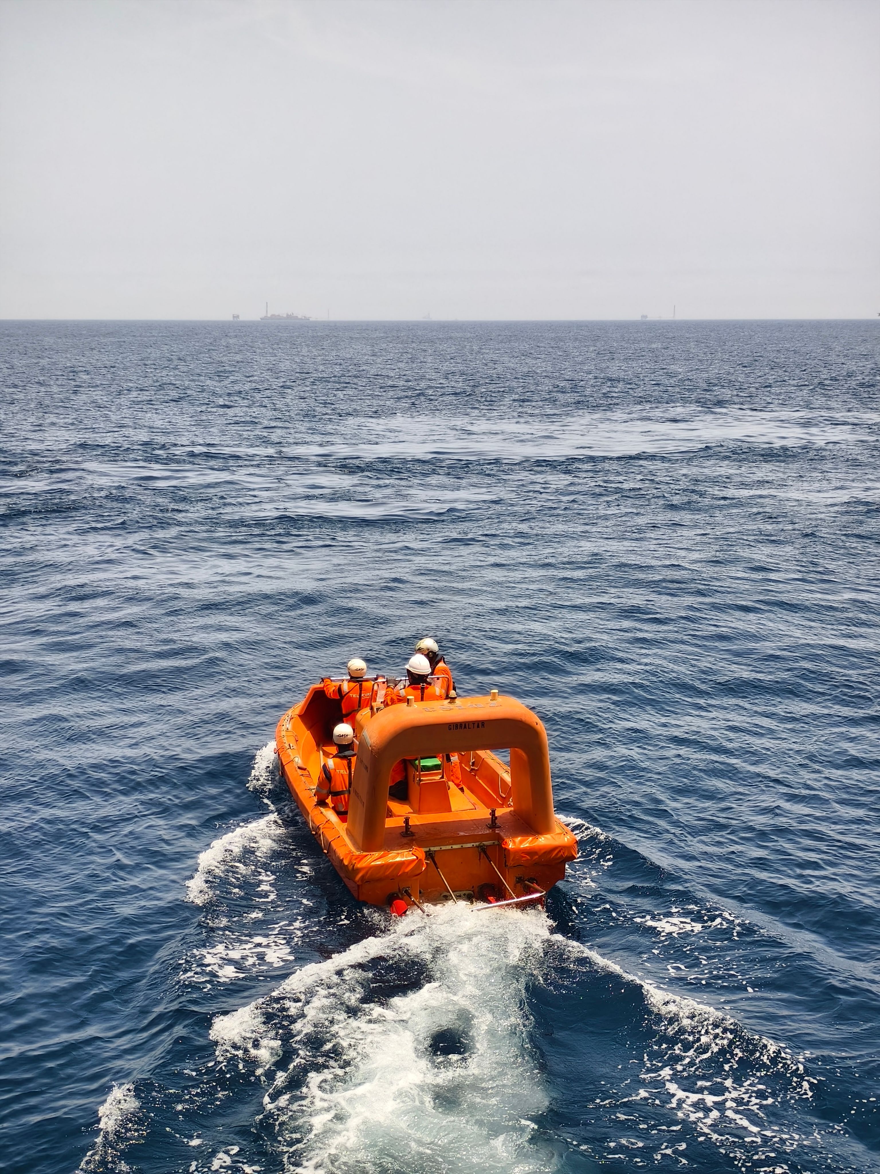 Een feloranje reddingsboot met bemanning vaart over de open oceaan en benadrukt veiligheid en avontuur.