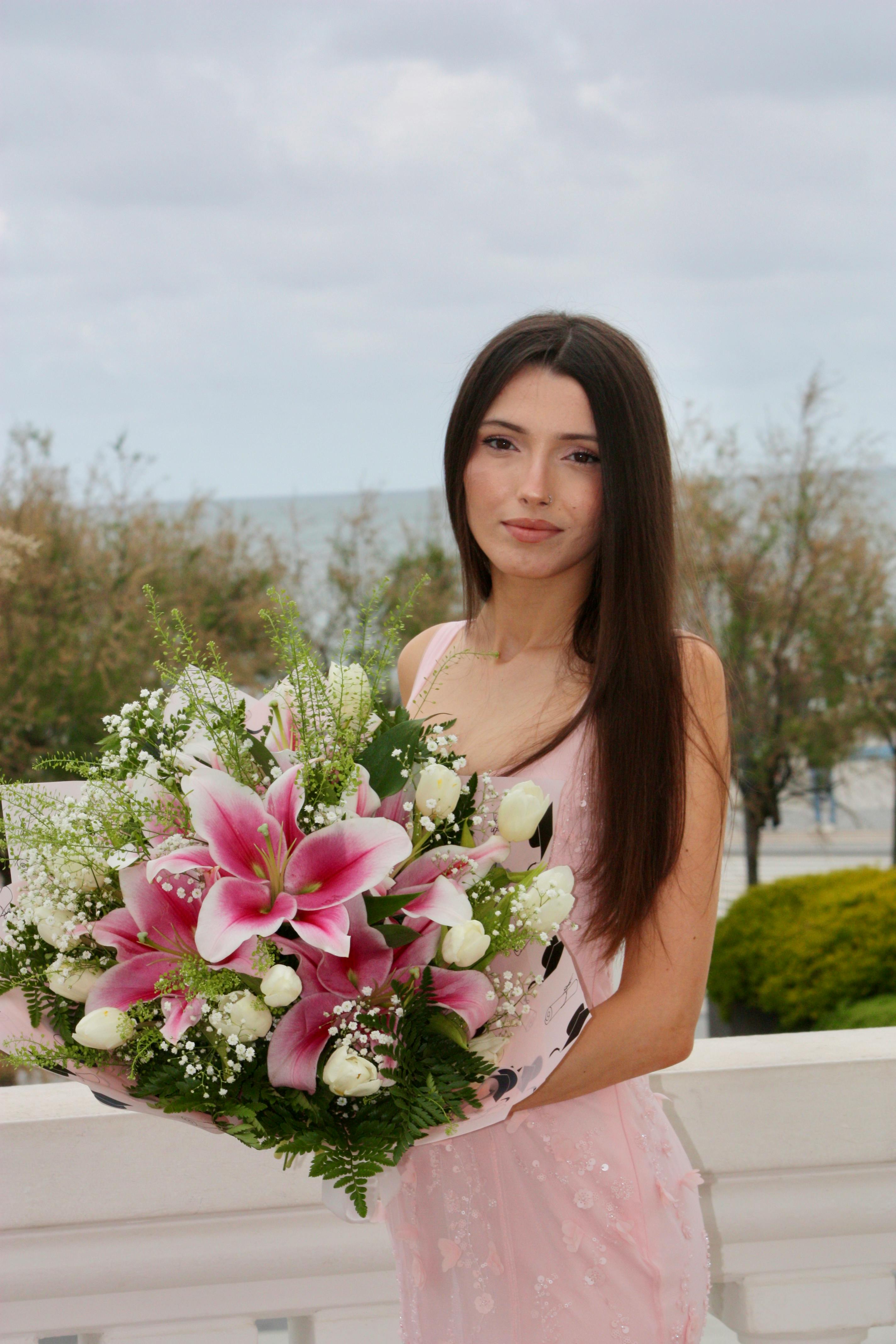 Young woman holding a pink flower bouquet outdoors near the ocean in Santander, Spain.
