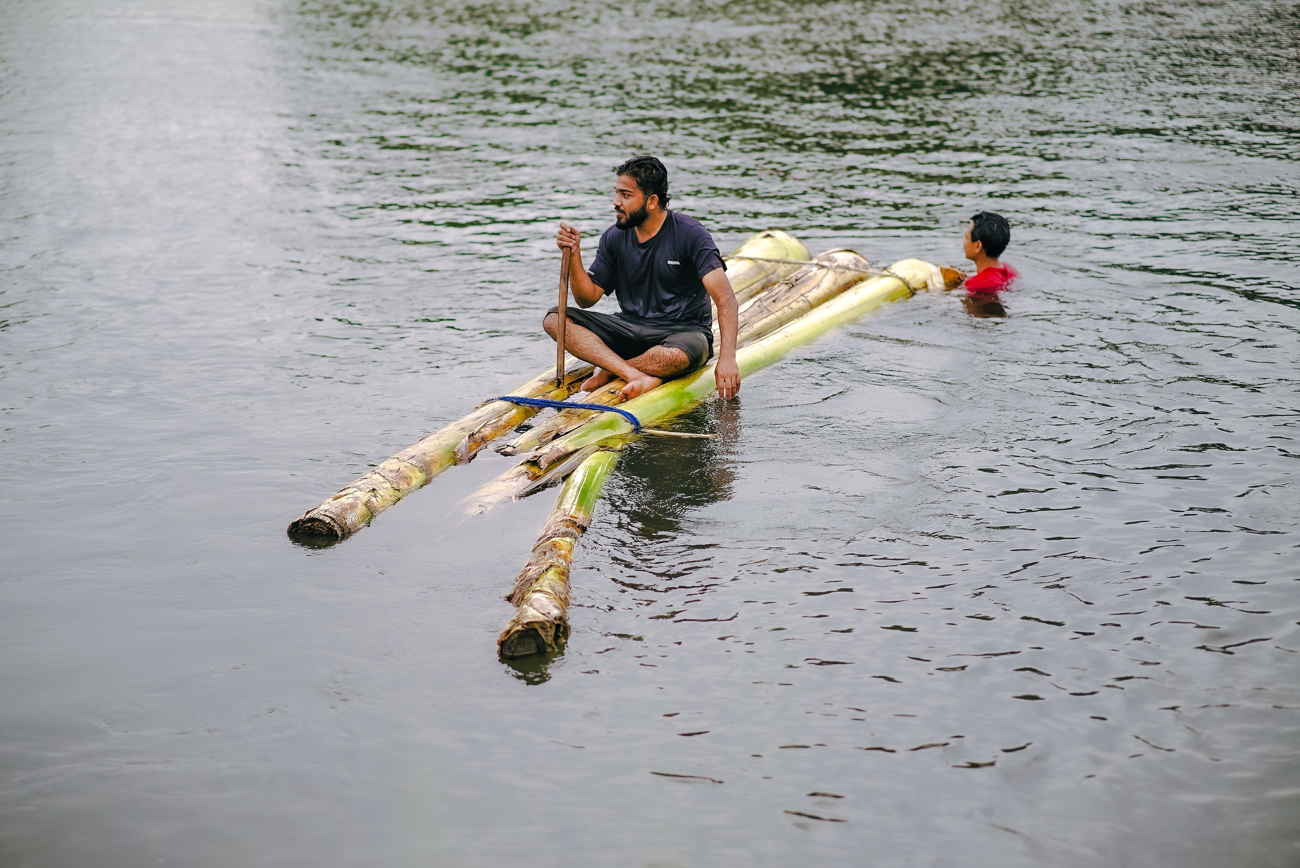 Two individuals navigating a river on a handmade bamboo raft, showcasing traditional watercraft.