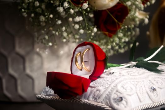 Close-up of wedding rings in a rose-shaped box, set against a floral bouquet backdrop.