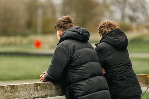Free Two individuals in black jackets leaning on a fence, gazing outward on a cloudy day. Stock Photo