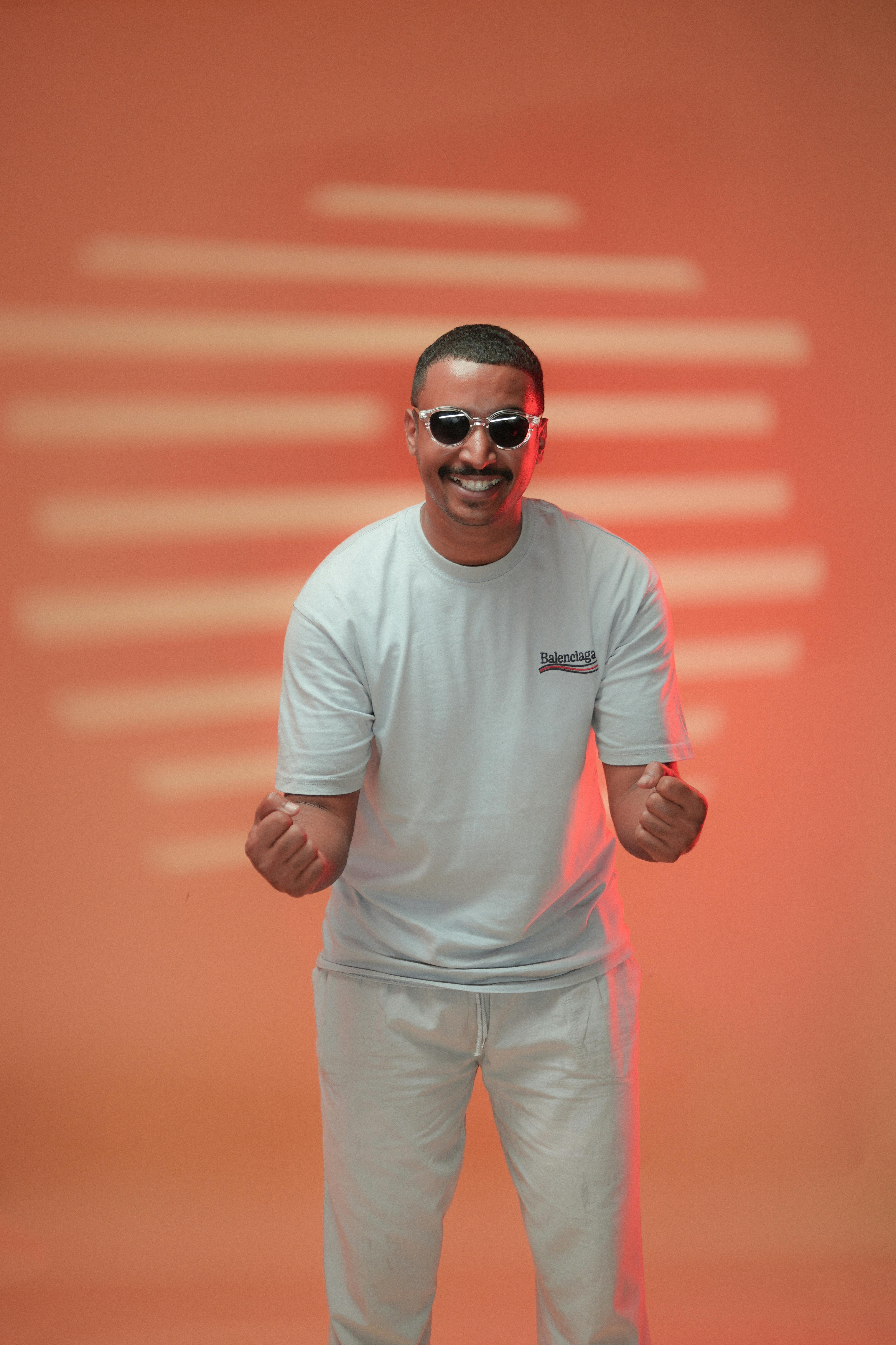 Cheerful man in white shirt and sunglasses poses against an orange background.