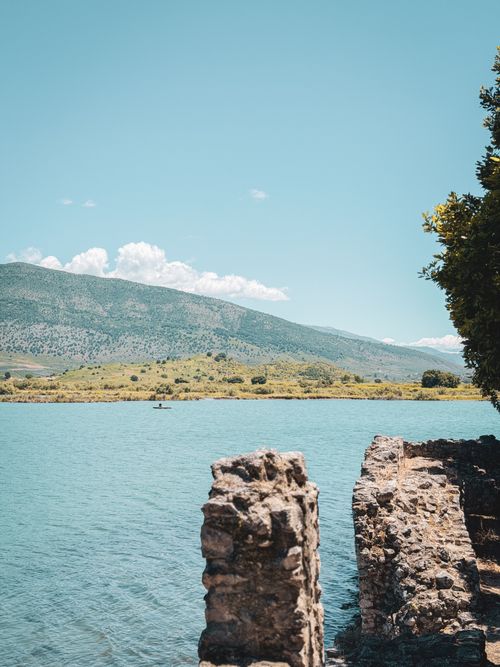 Free Serene lake landscape with distant hills, stone ruins, and clear blue sky. Stock Photo