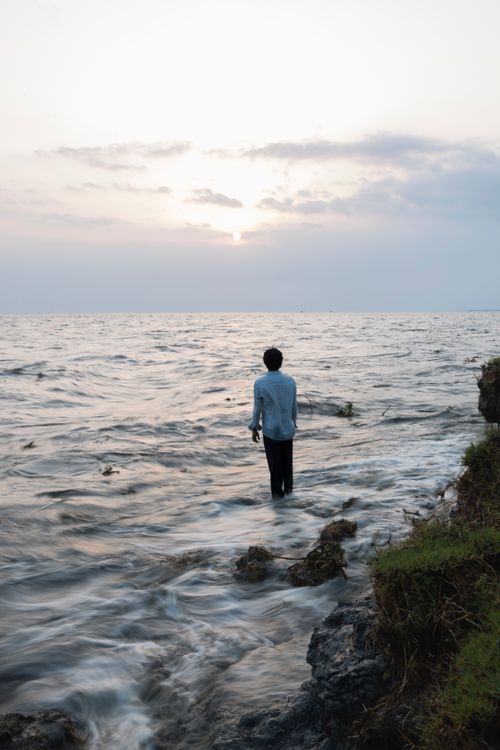 Man Standing on Rocky Shore at Sunrise · Free Stock Photo