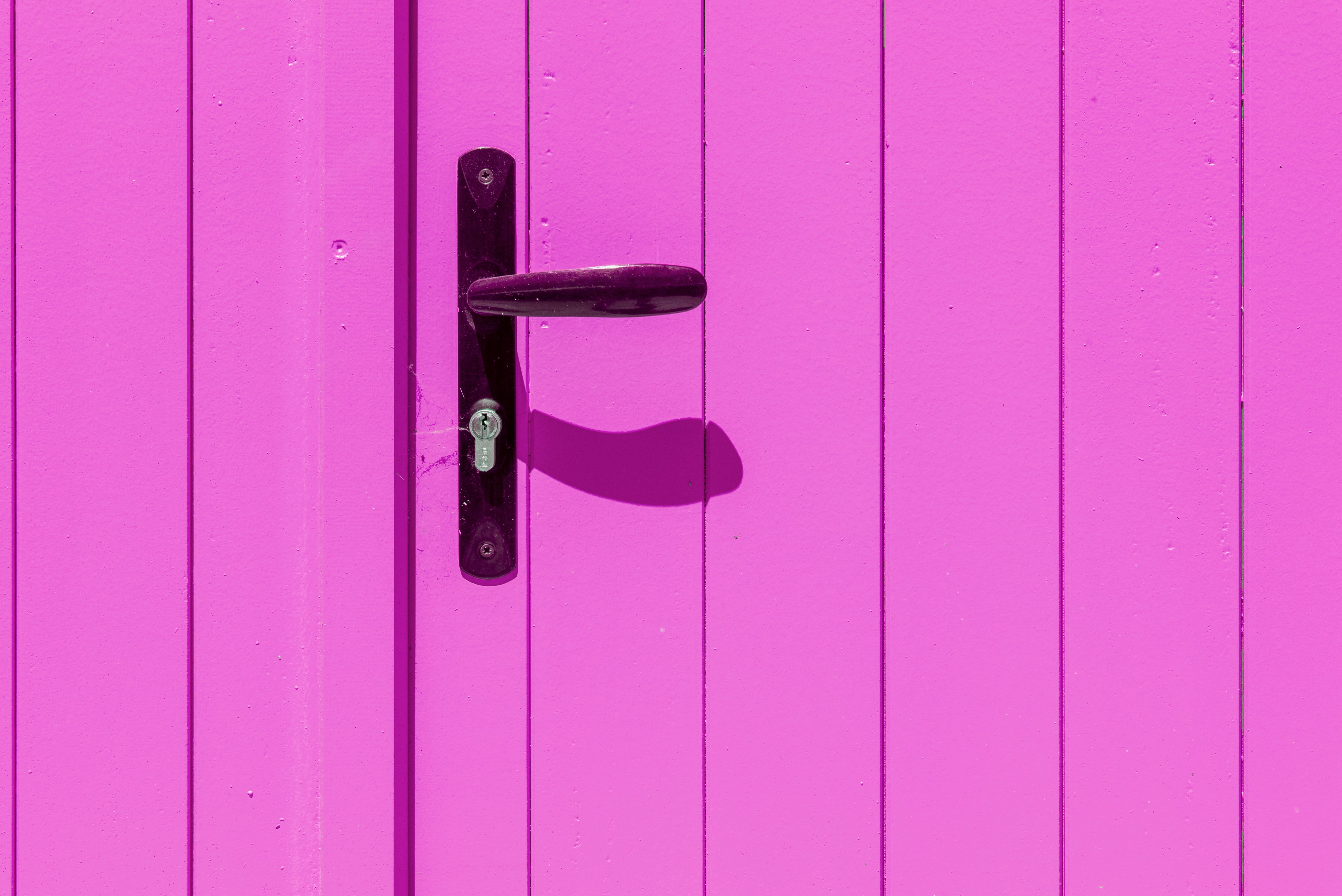 An eye-catching pink door with a black handle casting a sharp shadow, creating a vivid contrast — beginners unlocking for beginners