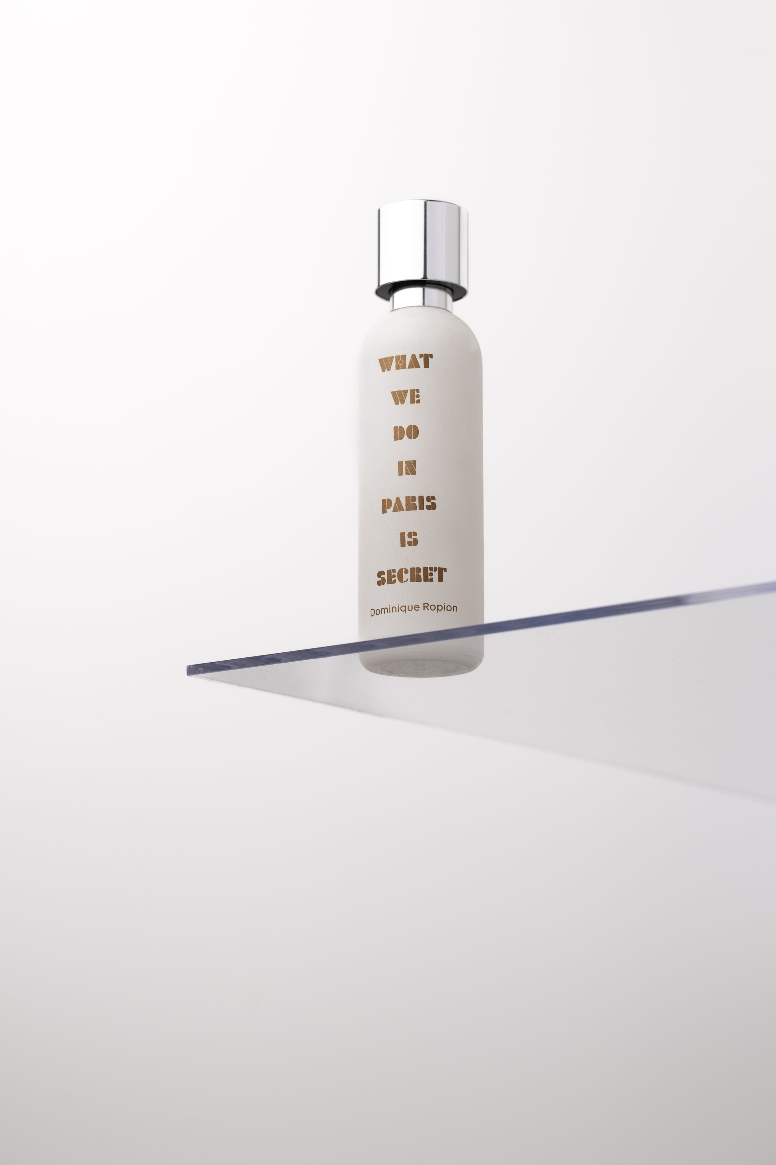 Elegant minimalist bottle with text, on a sleek glass shelf. Ideal for product advertising.
