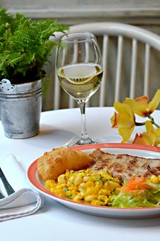 Plate of gourmet food with wine glass, flowers, and greenery on an elegant table setting.