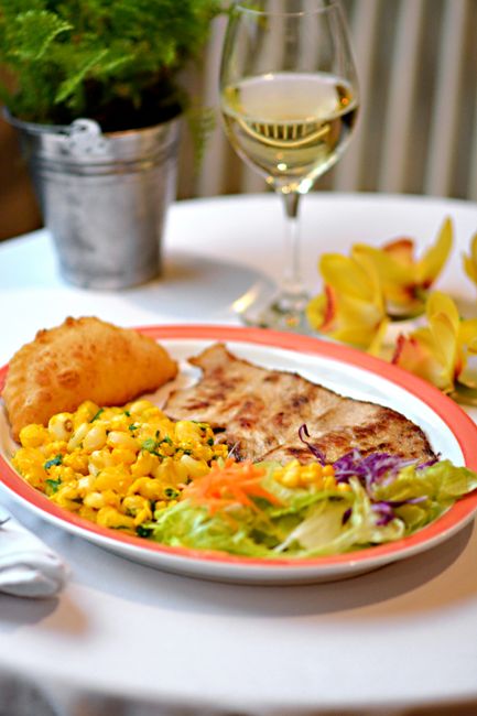 A delicious gourmet dinner featuring crispy fish, macaroni, fresh salad, and white wine on a table. - Oistins Fish Fry: Menu Prices, Best Stalls, and What to Expect