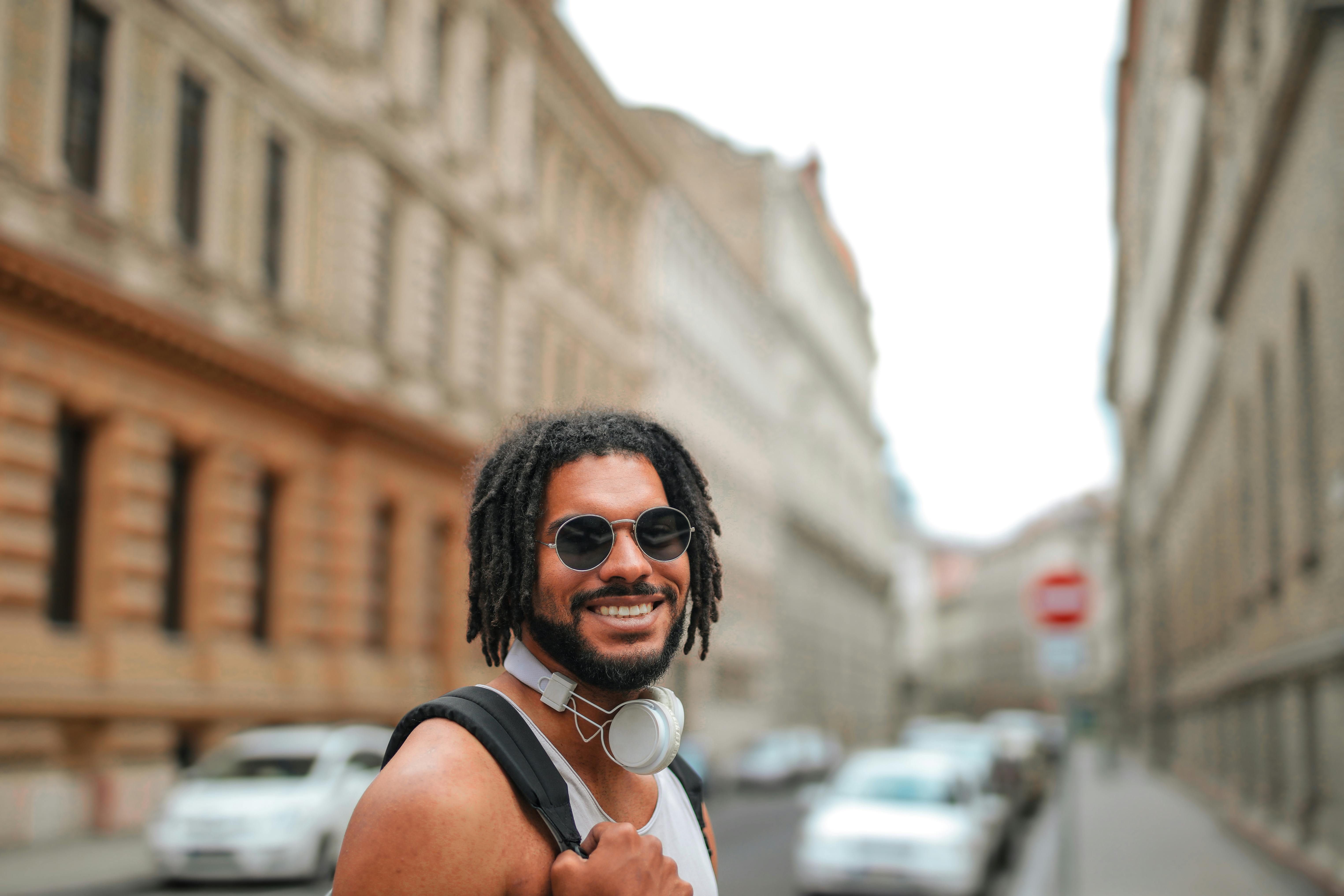 一个开朗的年轻人戴着墨镜和耳机，在繁忙的街道上微笑