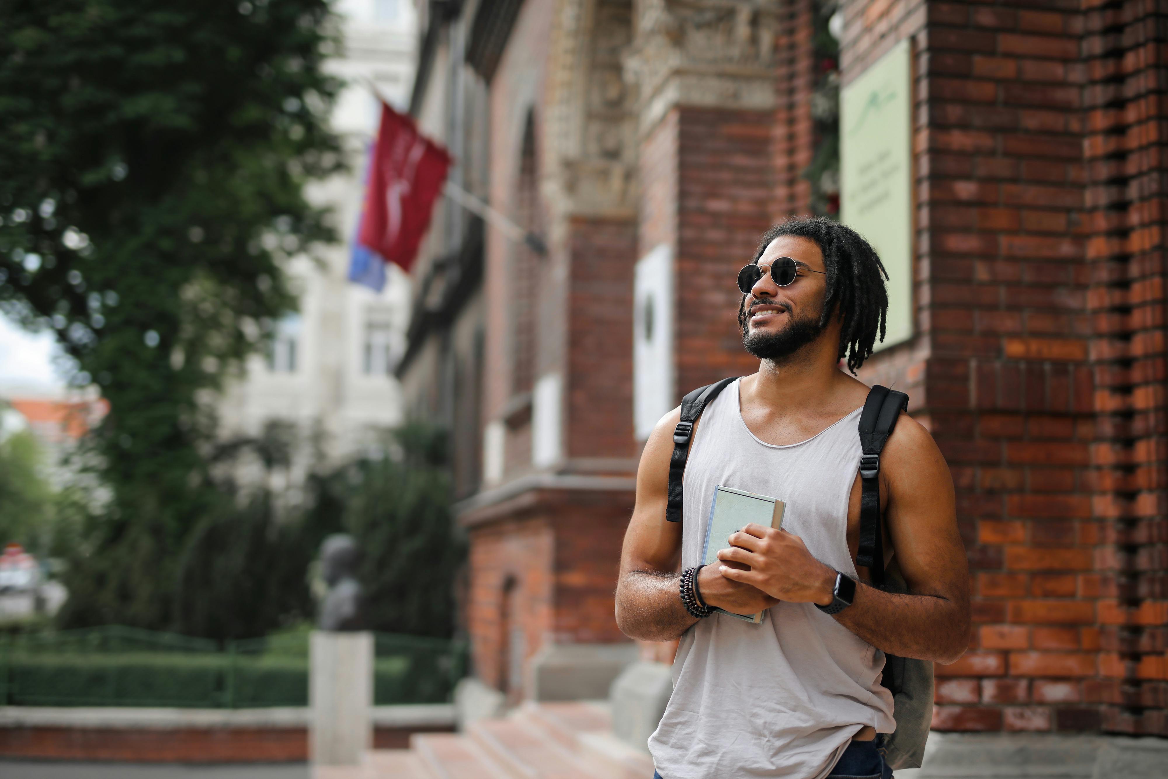 Smiling young man with dreadlocks and backpack enjoying a sunny day in the city.