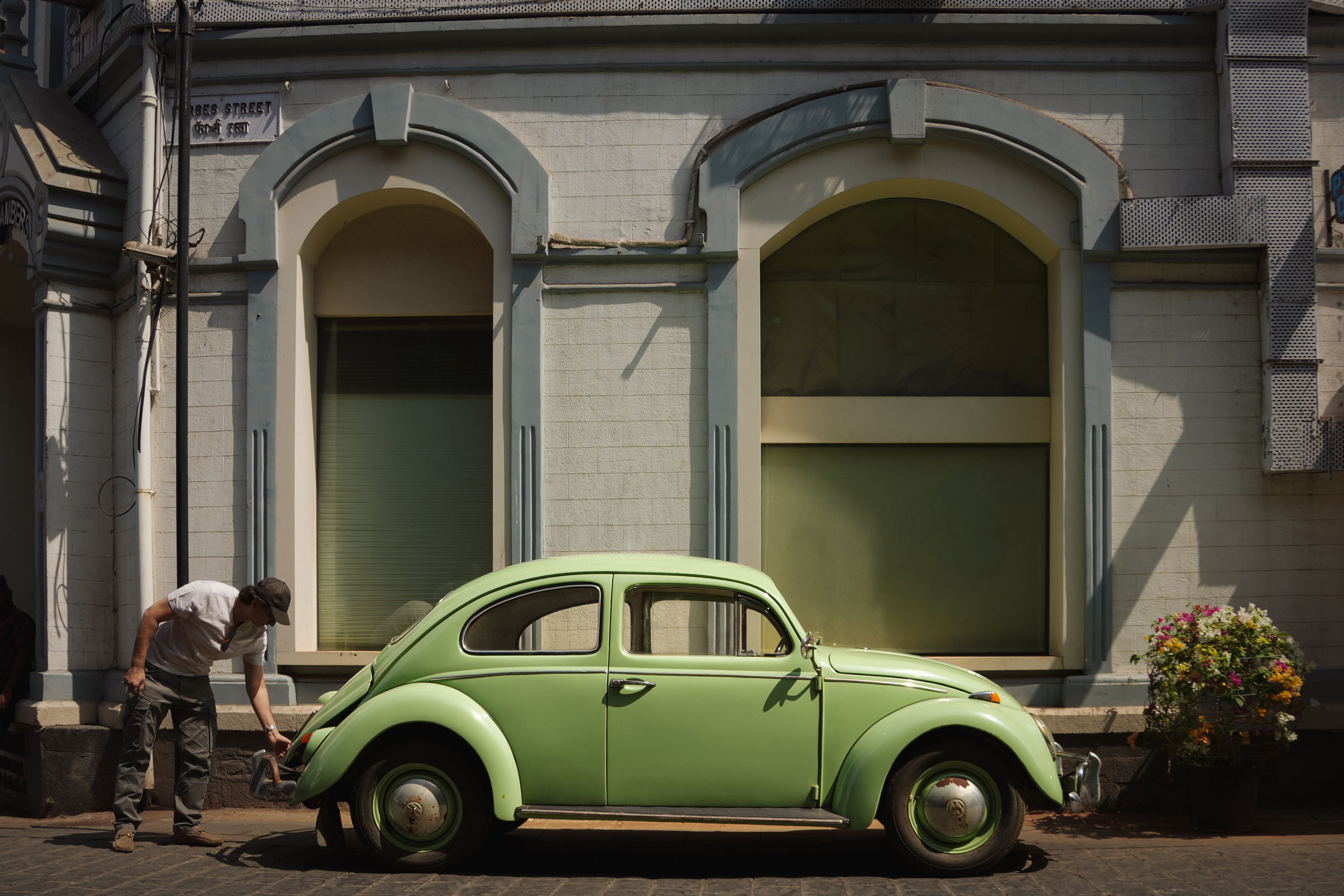 A vintage green car parked on an urban street with a person nearby, capturing a warm, retro vibe.
