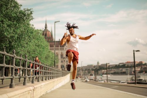 Free Vibrant young man with dreadlocks jumps energetically on an urban street in daylight. Stock Photo