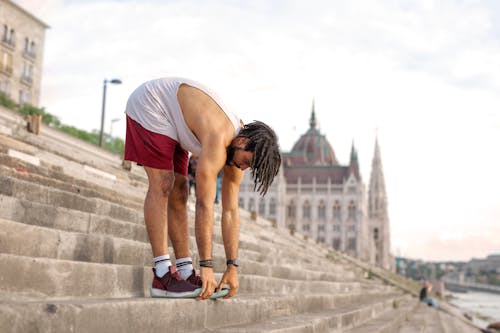 Man in White Tank Top and Red Shorts Stretching on Gray Concrete Stairs