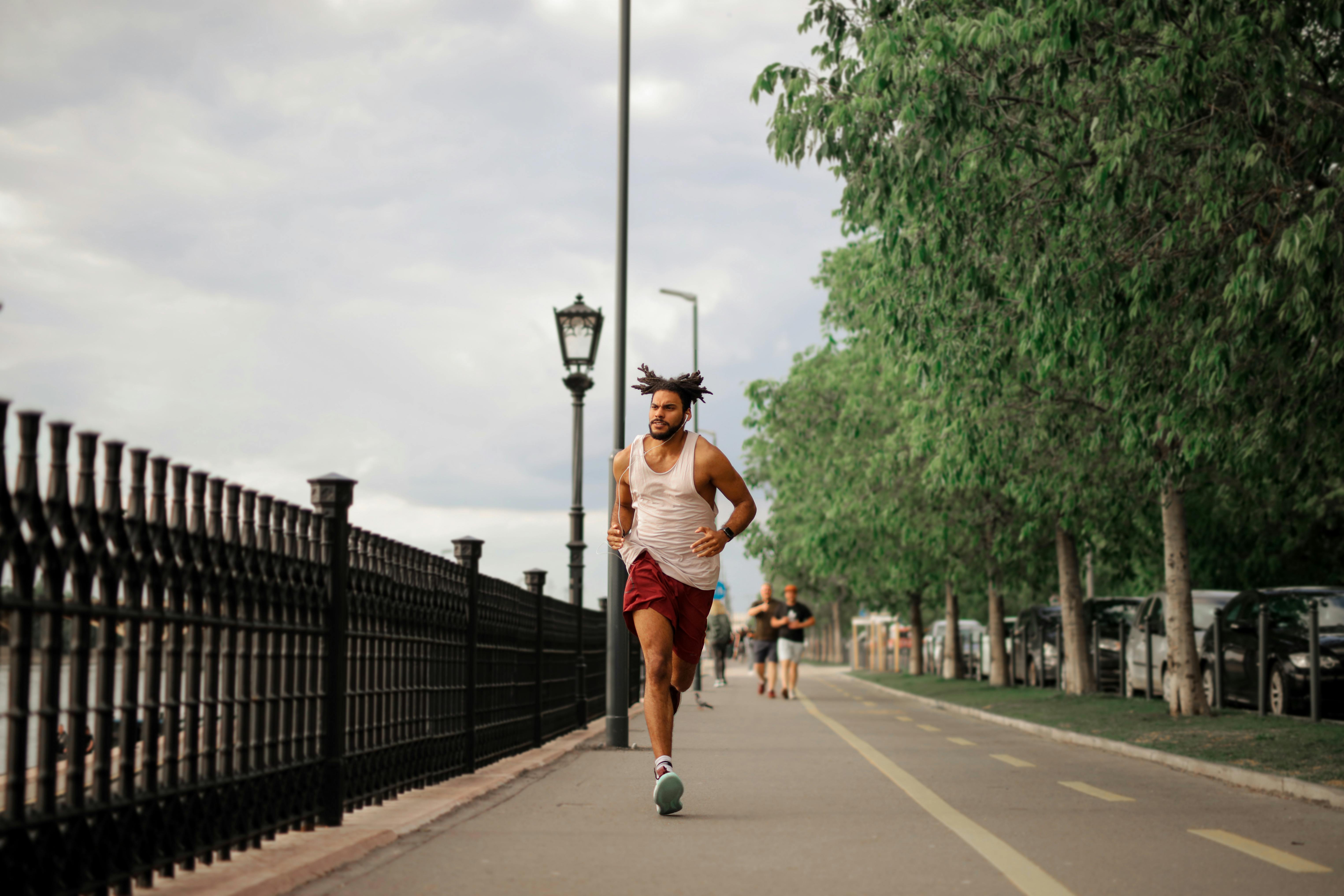 man in white tank top and red shorts running on road
