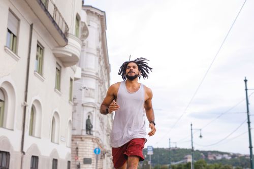 Free A young man jogging energetically on a city street with historic architecture in the background. Stock Photo