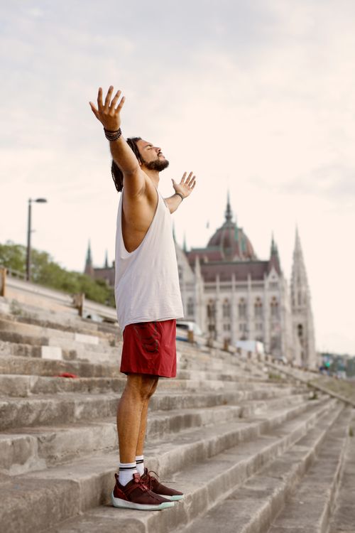 Free A young man stands on stone stairs, arms wide, embracing nature. Stock Photo