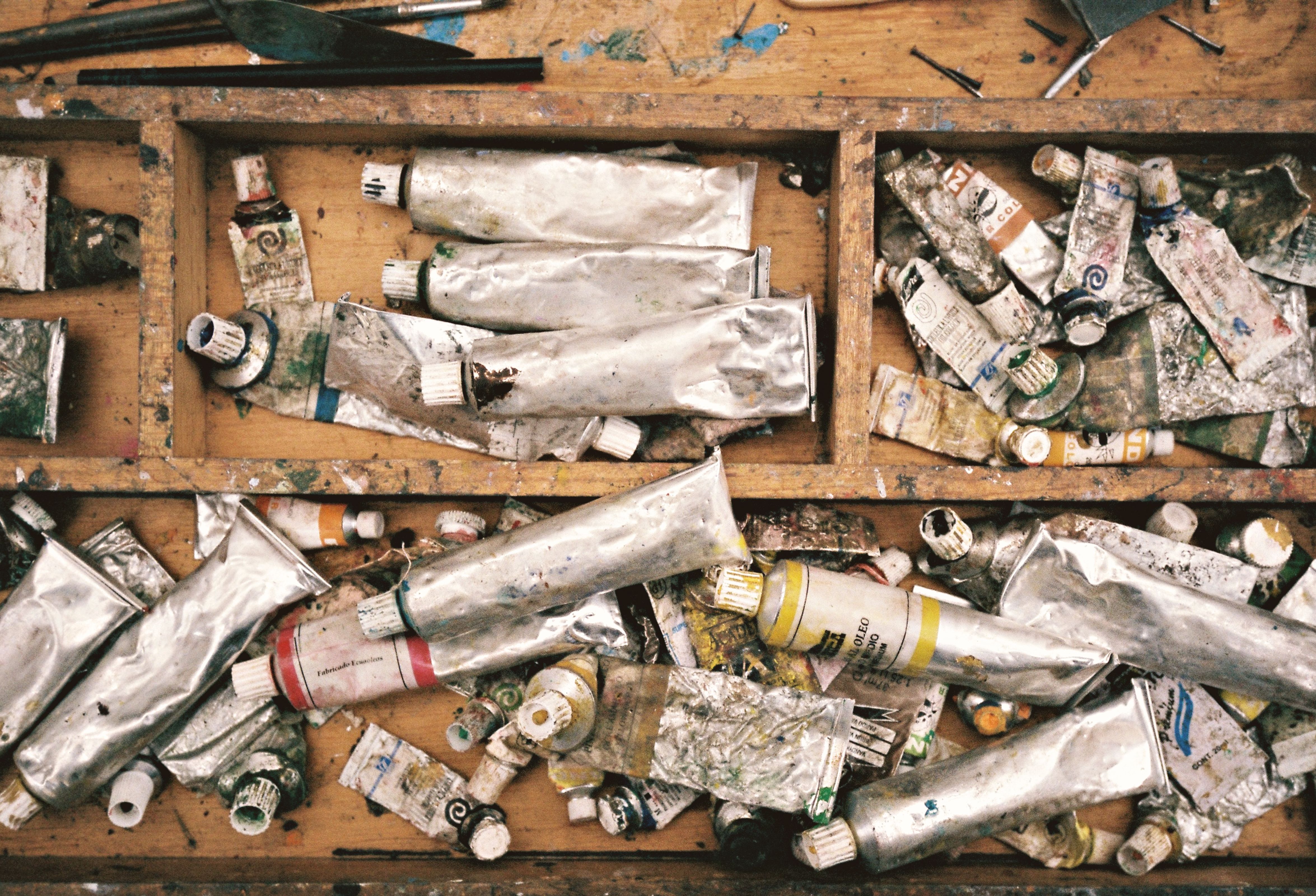 A top-down view of a cluttered artist's workspace filled with used paint tubes and brushes.