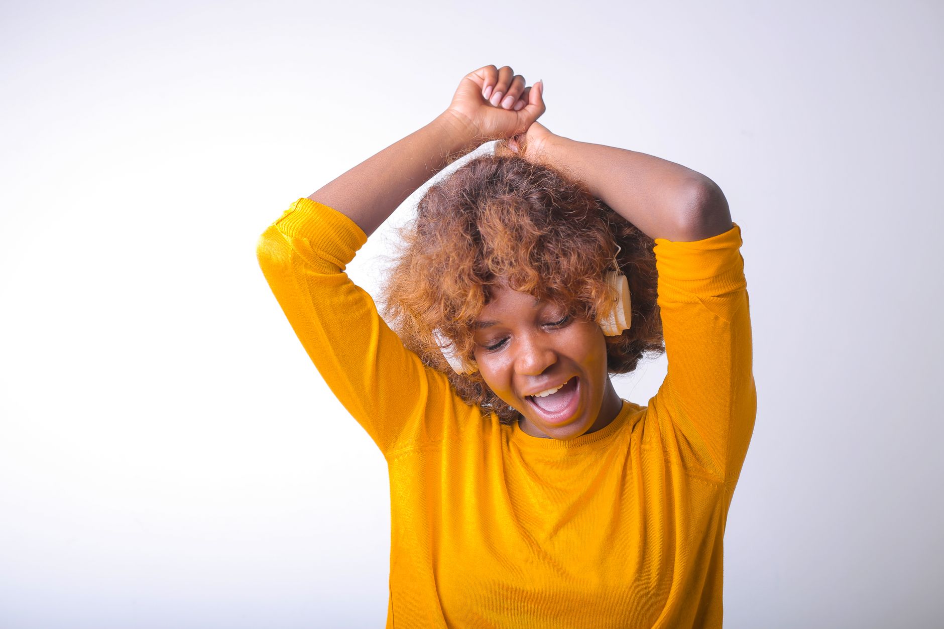 A cheerful woman in a bright yellow top listening to music with headphones, eyes closed in enjoyment.