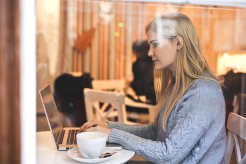 Free Serious young woman using netbook while having hot drink in modern cafe Stock Photo