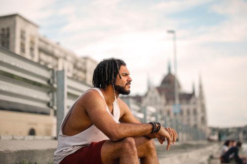 Free Man in casual attire sitting outdoors in a cityscape, enjoying a peaceful moment. Stock Photo