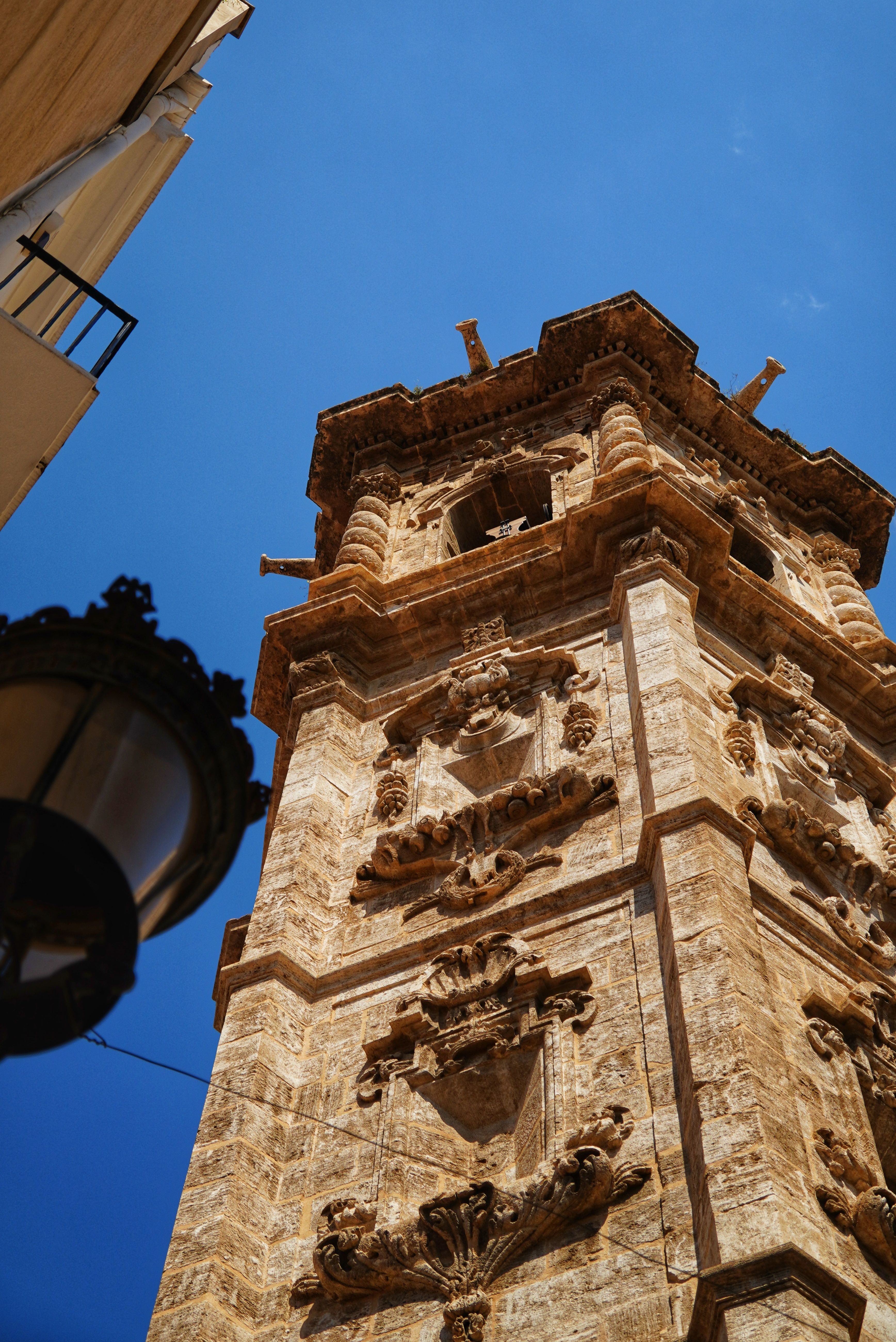 Ornate stone bell tower against a bright blue sky in Valencia, Spain.