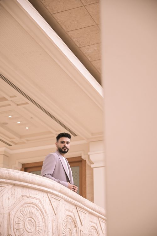 Free Adult male in a formal suit standing on an elegant indoor balcony with intricate designs. Stock Photo
