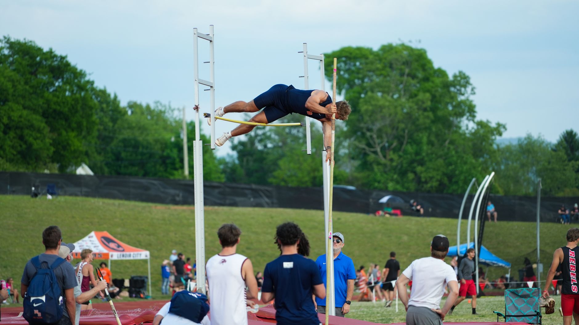 An athlete in action during a pole vault competition at an outdoor sports event with a crowd watching.