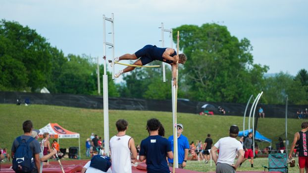 An athlete in action during a pole vault competition at an outdoor sports event with a crowd watching.