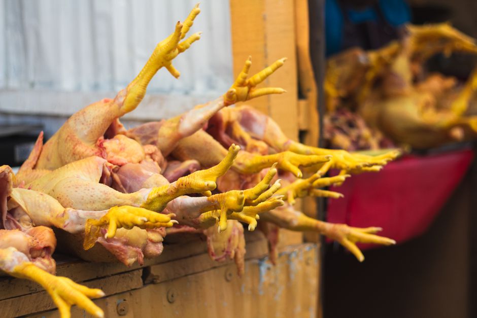A pile of cleaned raw chicken feet with pale yellow skin and trimmed nails on a wooden cutting board, ready for blanching.