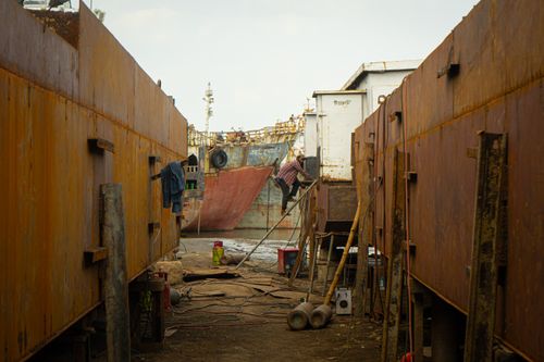 Free Industrial shipyard scene featuring a worker amidst rusted metal with scattered tools. Stock Photo
