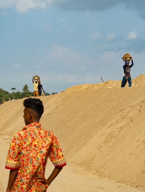 Free Laborers carry baskets of sand on a construction site with clear skies above. Stock Photo
