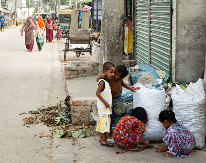 Young children play near a street market, surrounded by urban life in a bustling city.