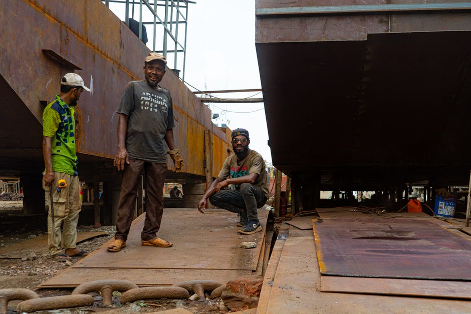 Men working at a shipyard construction site with large metal structures.