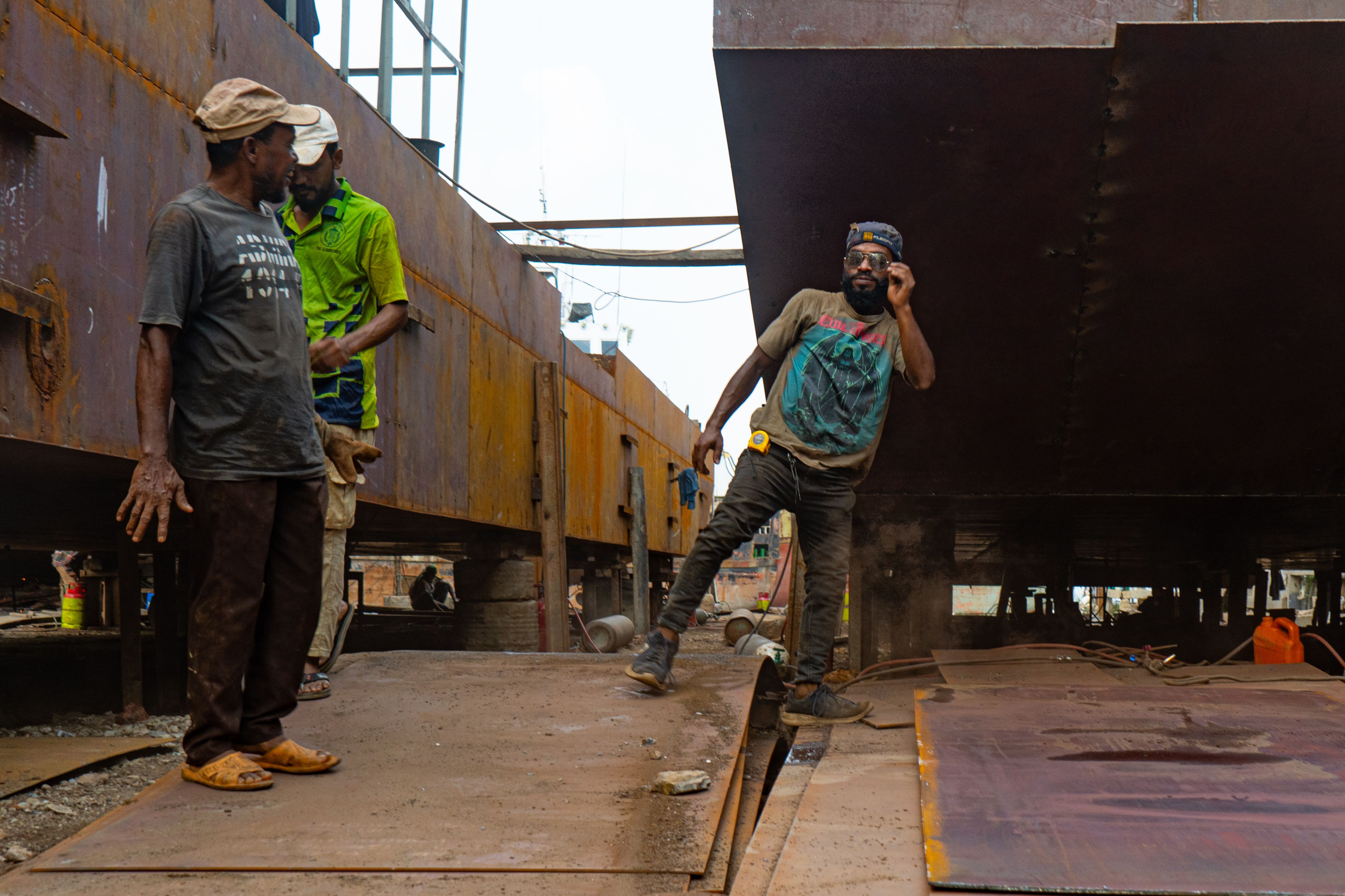 Men working on ship repairs at a shipyard with visible industrial equipment.