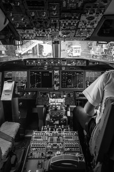 Monochrome image of a commercial airplane cockpit with a pilot, showcasing the detailed dashboard and controls.
