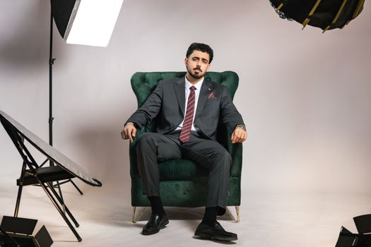 Businessman in suit seated in a studio chair, surrounded by lighting equipment.