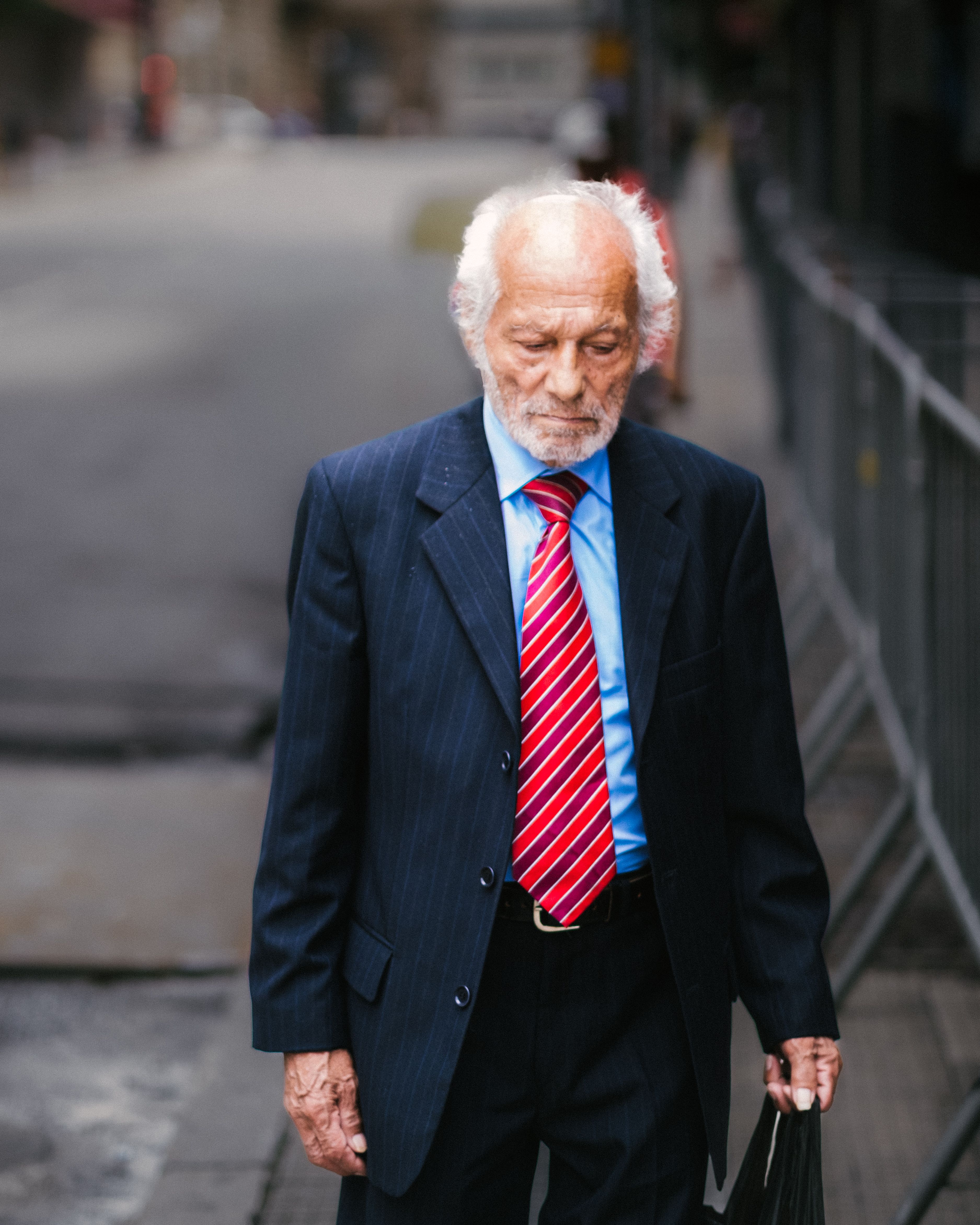 Elderly man in formal attire walks along a city street in São Paulo, Brazil.